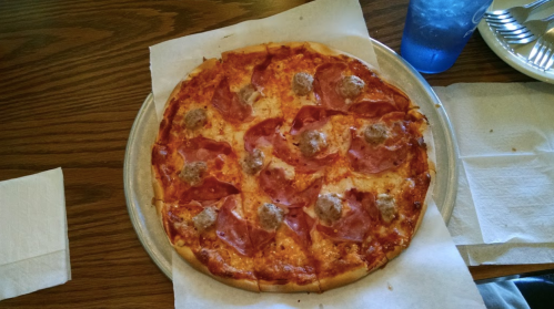 A round pizza topped with pepperoni and meatballs, served on a silver tray with napkins and a blue drink nearby.