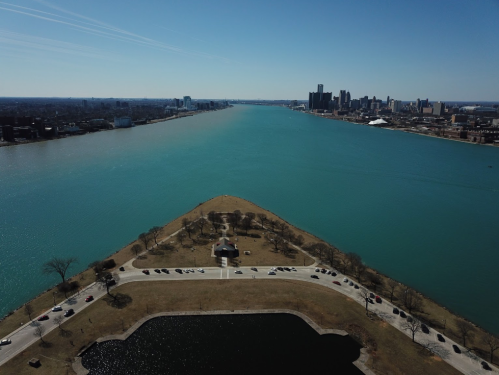 Aerial view of a river splitting into two, with a park and city skyline in the background on a clear day.