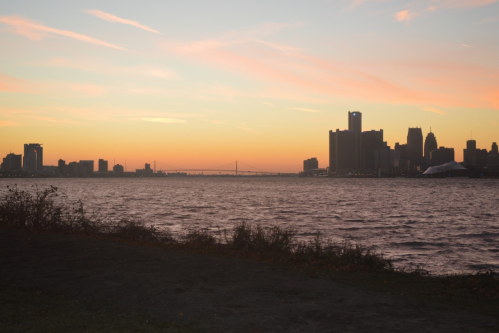 Silhouette of a city skyline at sunset, with a river in the foreground and colorful clouds in the sky.