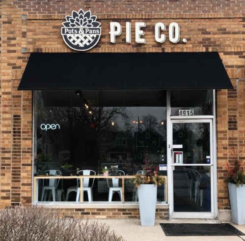 Exterior of Pots & Pans Pie Co. featuring a large window, "open" sign, and a welcoming atmosphere.
