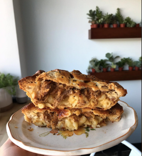 A close-up of a cheesy sandwich filled with pulled pork and macaroni, served on a decorative plate.