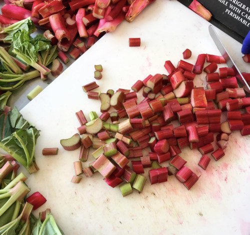 Chopped rhubarb pieces on a cutting board, surrounded by whole rhubarb stalks and leafy greens.