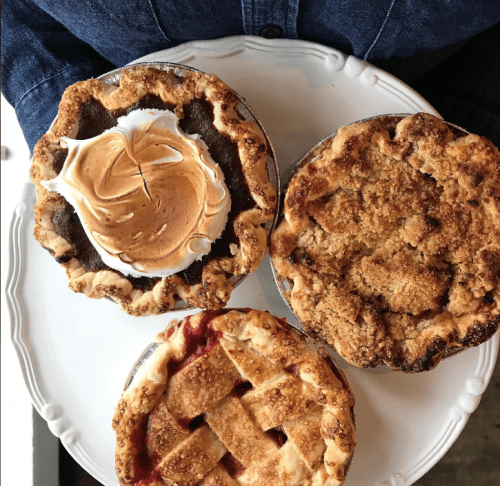A white plate holding three delicious pies: chocolate meringue, apple crumble, and cherry lattice.