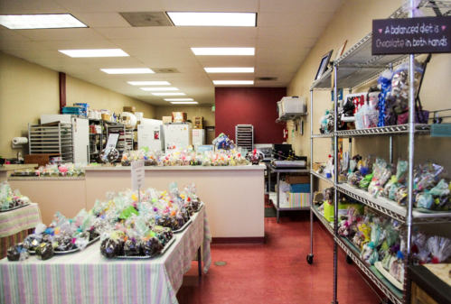 A colorful candy shop interior with tables of wrapped treats and a kitchen area in the background.