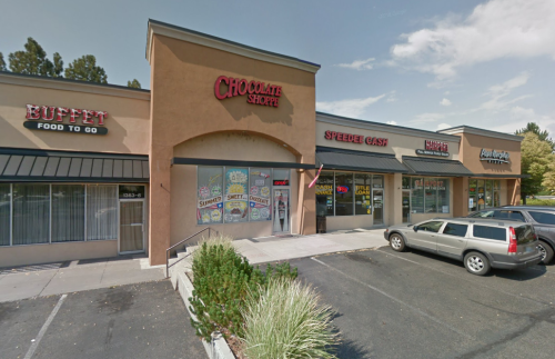 A storefront featuring "Chocolate Shoppe" and "Speedee Cash" in a shopping plaza with parked cars and greenery.