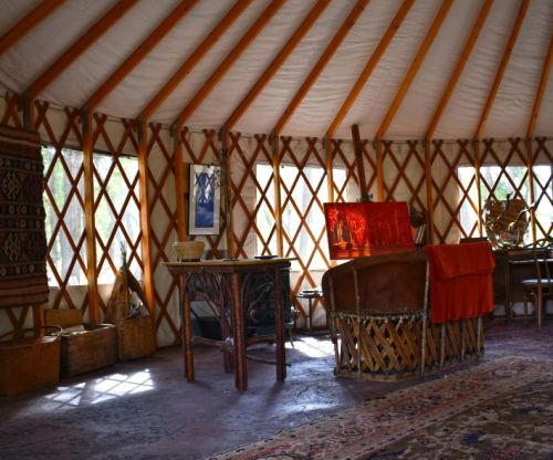 Interior of a yurt featuring wooden beams, a table, decorative rugs, and warm lighting.