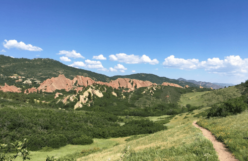 A scenic view of red rock formations surrounded by green hills and a blue sky with fluffy clouds.