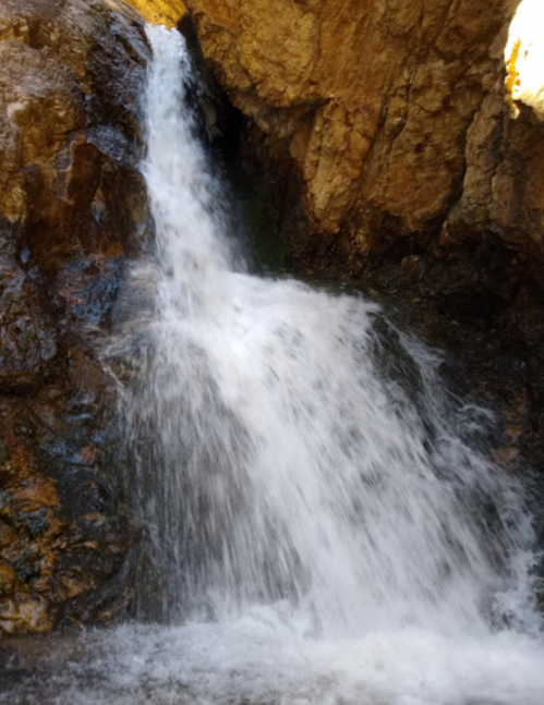 A cascading waterfall flows over rocky terrain, surrounded by natural stone formations.