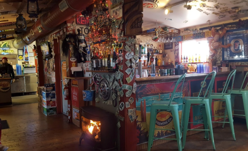A cozy bar interior with colorful decor, a fireplace, and a variety of bottles on the shelves.