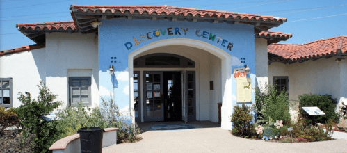 Entrance of the Discovery Center featuring a colorful sign, arched doorway, and surrounding greenery.