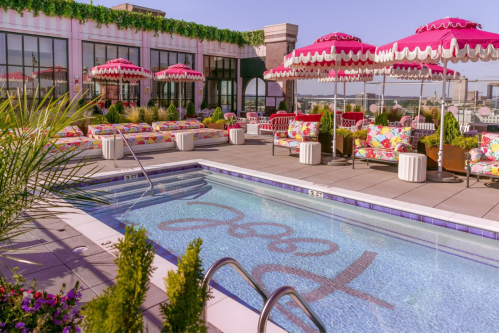 Rooftop pool area with colorful lounge chairs, umbrellas, and greenery, overlooking a scenic view.