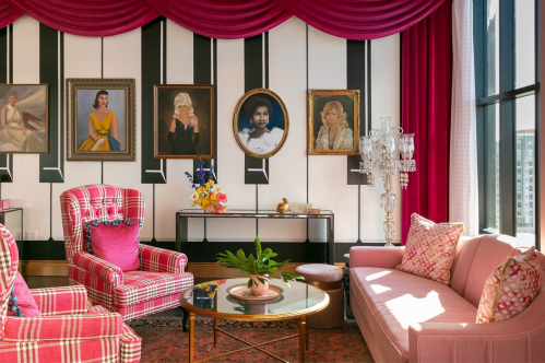 A stylish living room with pink furniture, framed portraits on the wall, and a decorative chandelier.