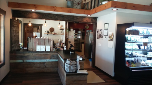 Cozy café interior featuring a wooden counter, shelves, and a display fridge filled with various food items.