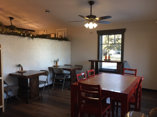 Cozy dining area with wooden tables, red chairs, and a ceiling fan, featuring a bright window and decorative plants.