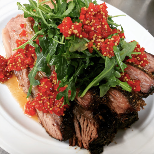 A plate of sliced beef topped with arugula and a vibrant red pepper sauce.