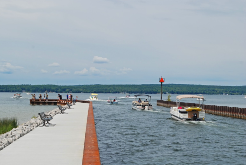 A scenic view of a marina with boats navigating a waterway, surrounded by greenery and a cloudy sky.