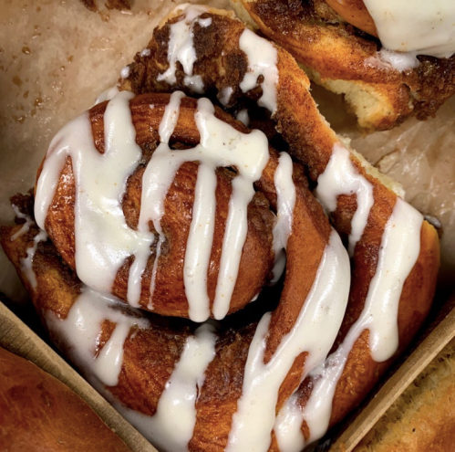 Close-up of a cinnamon roll drizzled with white icing, resting on parchment paper.