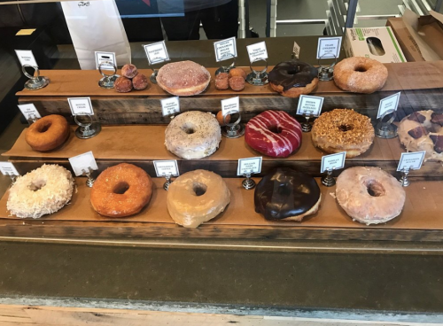 A display of various donuts on a wooden stand, featuring different flavors and toppings, with labels for each.