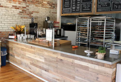 A rustic café counter with a wooden front, menu boards, and baked goods displayed on racks.