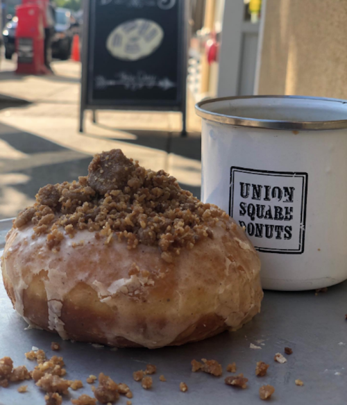 A glazed donut topped with crumbled topping next to a cup labeled "Union Square Donuts."