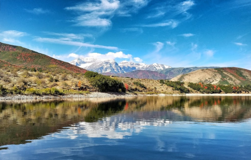 A serene lake reflects mountains and colorful autumn foliage under a clear blue sky.