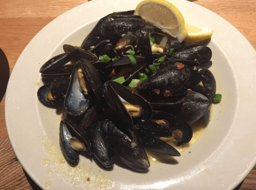A plate of mussels garnished with lemon and green onions, served in a flavorful broth.