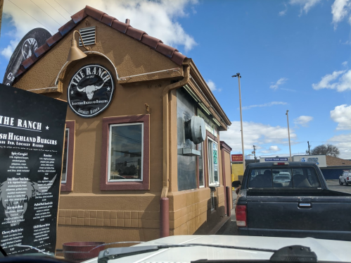 A drive-thru restaurant called "The Ranch" with a menu board and a pickup truck waiting in line.