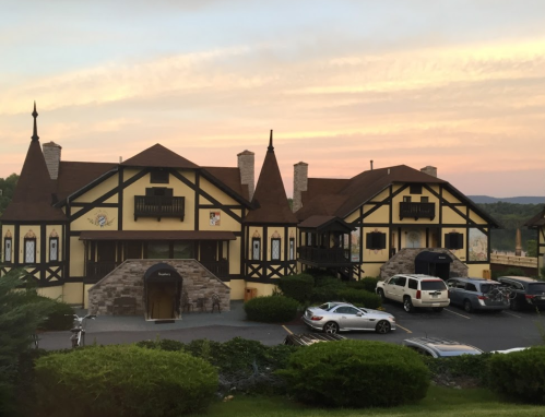 A charming, Tudor-style building with a sunset backdrop, surrounded by greenery and parked cars.