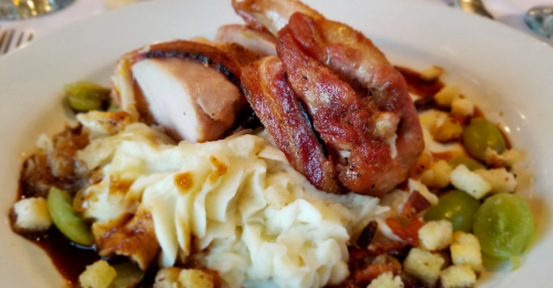 A plate of mashed potatoes topped with crispy chicken, bacon, croutons, and drizzled with sauce.