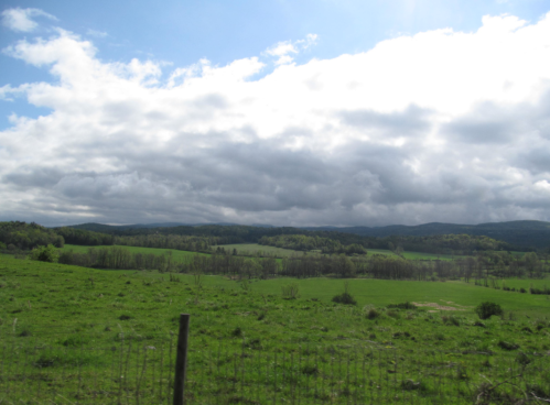 Lush green fields and rolling hills under a cloudy sky, with patches of sunlight breaking through.