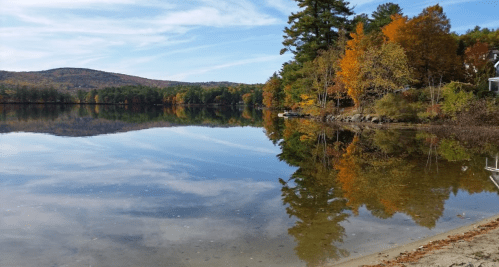 A serene lake reflecting vibrant autumn trees and a clear blue sky, with gentle ripples on the water's surface.