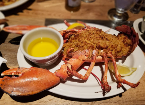 A plate featuring a whole lobster with stuffing, accompanied by a small bowl of melted butter and lemon wedges.