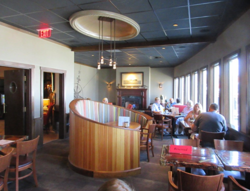 Interior of a restaurant featuring a curved booth, tables, and large windows with diners enjoying their meals.