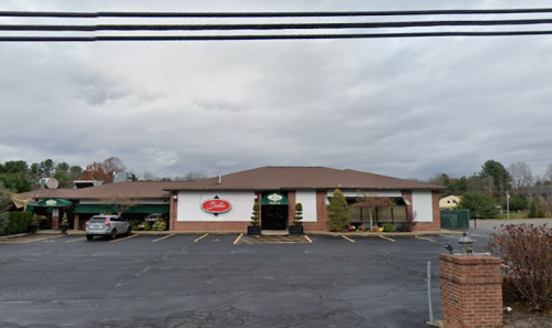 A single-story restaurant with a brown roof and signage, surrounded by a parking lot and cloudy sky.