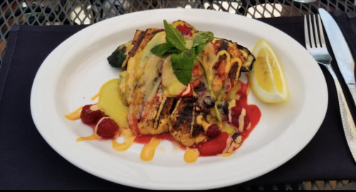Grilled fish fillet topped with sauce, garnished with mint and lemon, served on a white plate with berries.