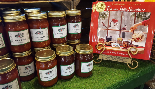 Jars of peach salsa on display next to a book titled "Tea with Lady Sapphire" in a cozy setting.
