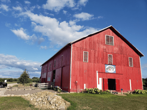 A large red barn with a sign, surrounded by green grass and a blue sky with scattered clouds.