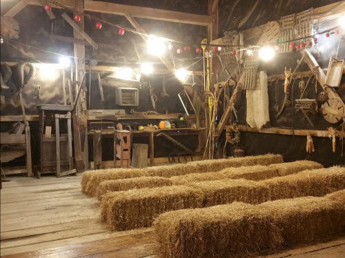 A rustic barn interior with straw bales, wooden tools, and warm lighting creating a cozy atmosphere.
