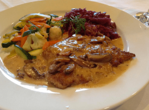 A plate featuring breaded fish in creamy mushroom sauce, served with sautéed vegetables and red cabbage.