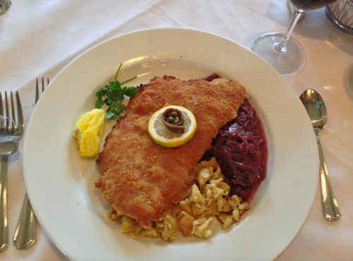 A plate of fried fish with a lemon slice, served with red cabbage and a side of noodles, garnished with herbs.