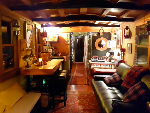 Cozy interior of a rustic cabin with wooden beams, a sofa, dining area, and warm lighting.