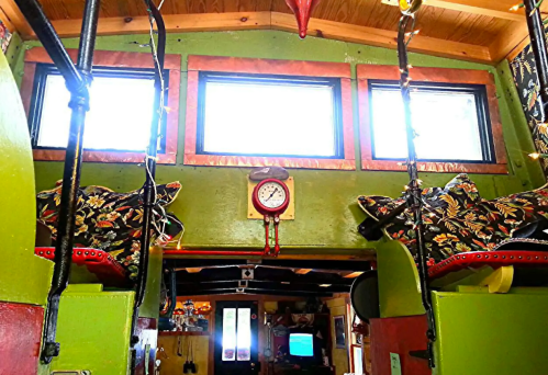 Interior of a colorful tiny home with green walls, large windows, a clock, and decorative cushions on either side.