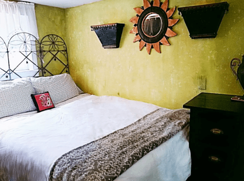 Cozy bedroom with a bed, decorative wall mirrors, and a textured yellow wall.