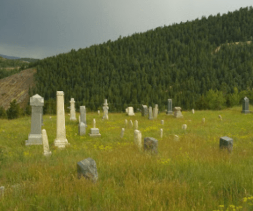 A serene cemetery with various gravestones set against a backdrop of green hills and a cloudy sky.
