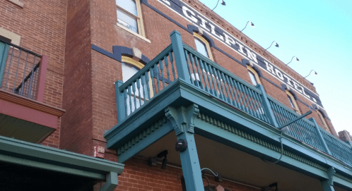 Exterior view of the Gilpin Hotel, featuring a wooden balcony and brick facade with string lights above.