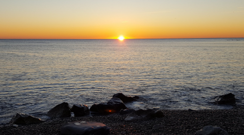 A serene beach scene at sunset, with the sun dipping below the horizon and gentle waves lapping at the shore.