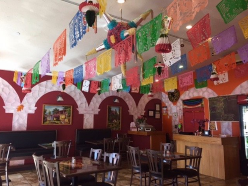 Colorful papel picado decorations hang from the ceiling of a vibrant restaurant with wooden tables and arches.