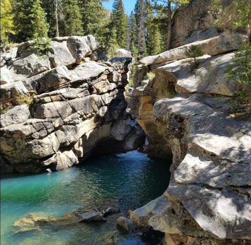 A serene natural scene featuring a narrow canyon with smooth rocks and clear turquoise water flowing through.