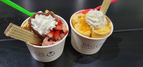 Two ice cream cups: one with chocolate, strawberries, and whipped cream; the other with rolled ice cream, caramel, and whipped cream.