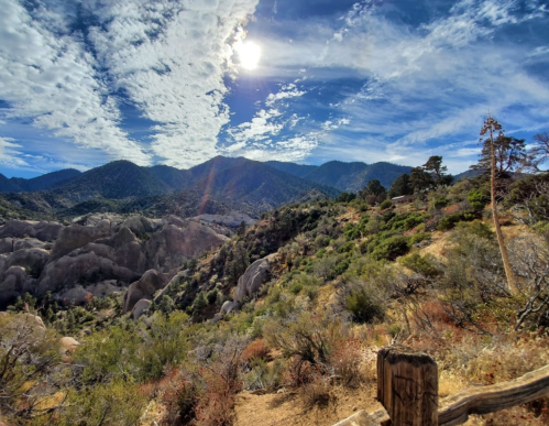 A scenic view of mountains and rocky terrain under a bright sky with scattered clouds. Sunlight illuminates the landscape.
